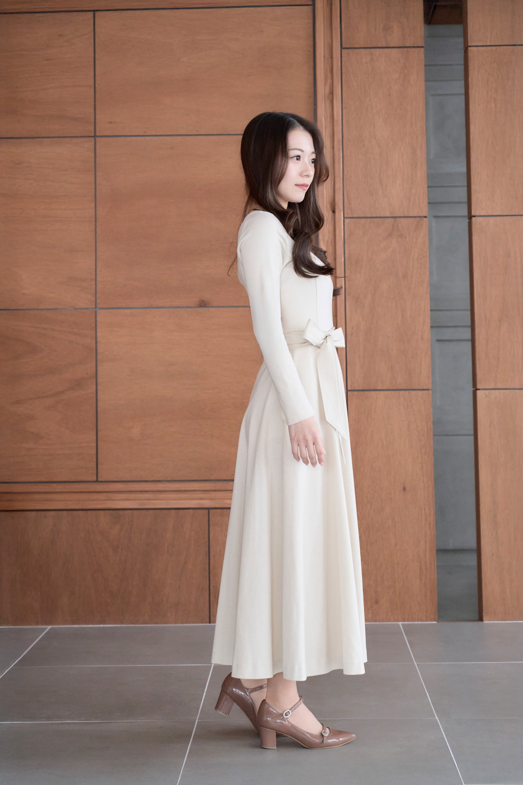 ベージュ色のリボン付き低身長ワンピースを着用した横姿